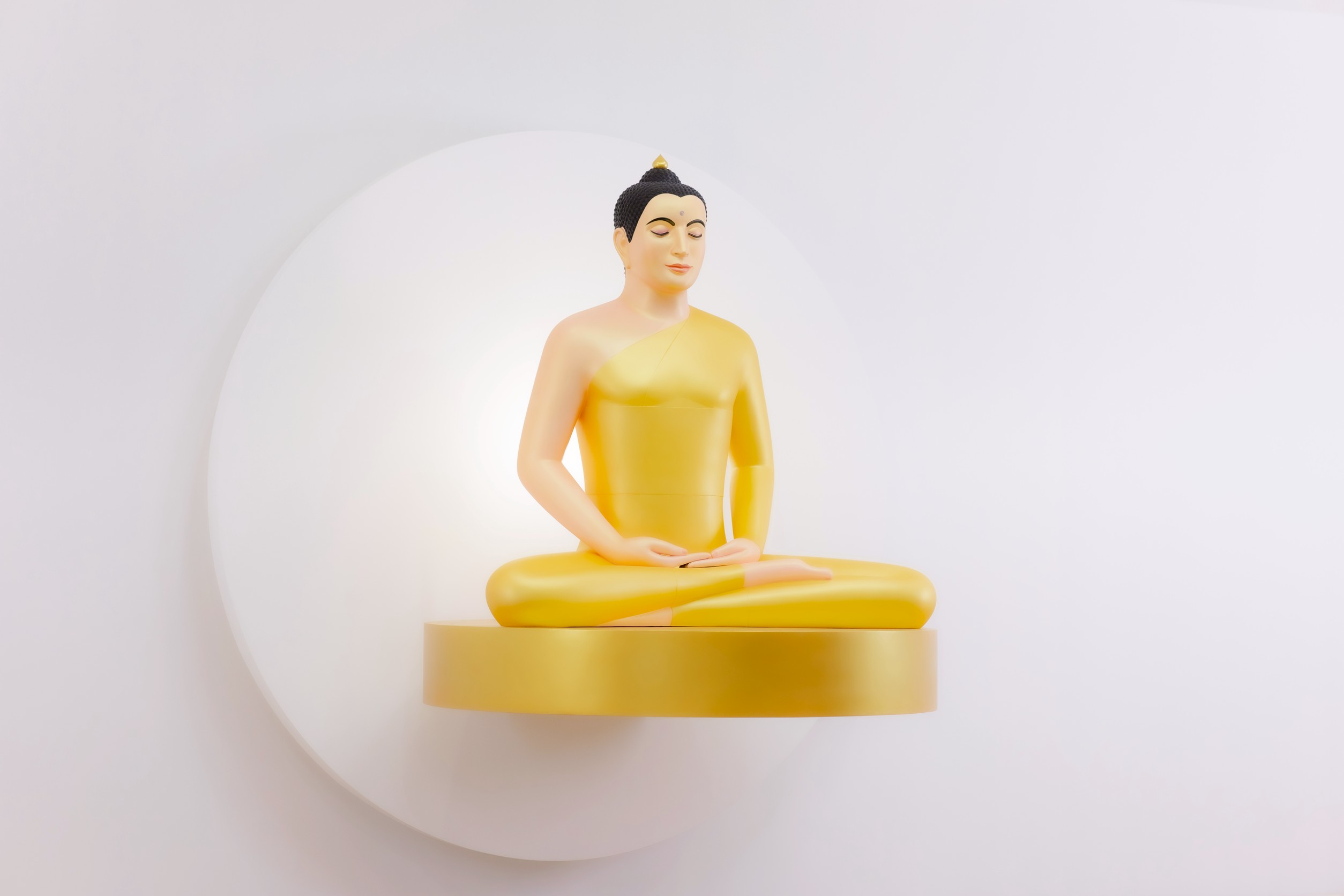 The principal Buddha image mounted on a white circular backdrop disc that stands proud of the wall, seated on a gold base disc that cantilevers out from it